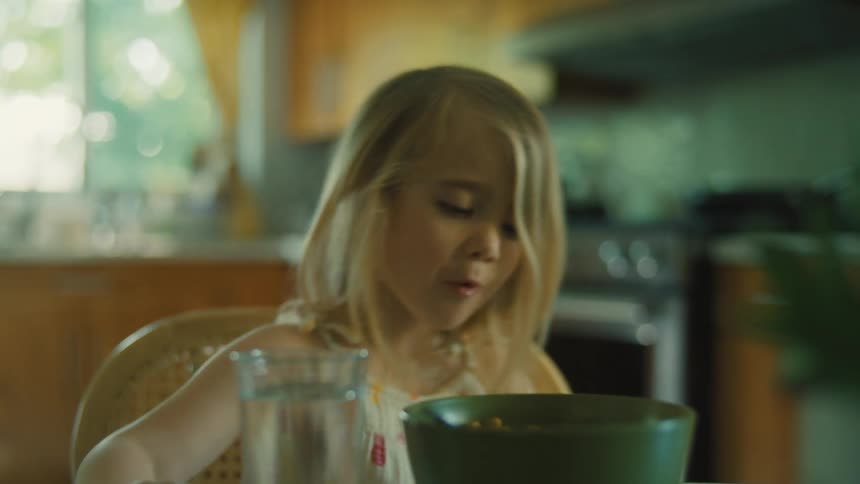 The first video shows a little girl sitting at a kitchen table drinking a glass of water and eating from a bowl the second video shows a person kitesurfing across the water using a large kite to pull them on a board