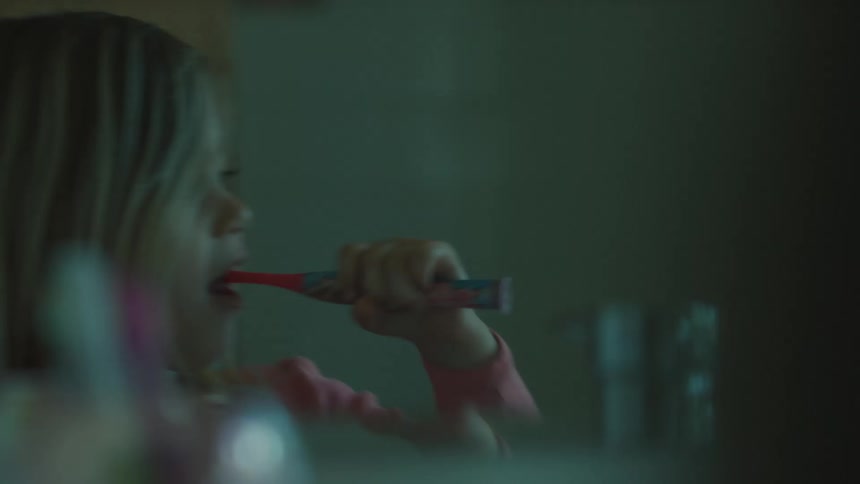 A young blonde girl brushes her teeth at a sink