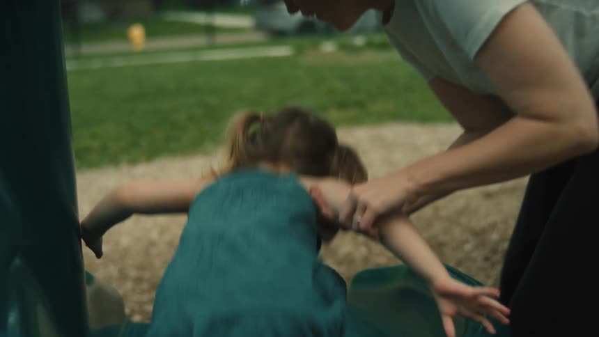 A young girl smiles as she comes down a slip and slide and an older woman picks her up at the bottom after which the girl runs in another direction