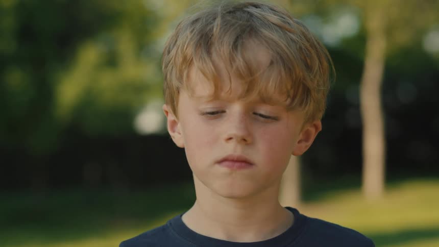 The video shows a closeup of a young boy with lightcolored hair looking directly at the camera he blinks slowly and has a serious expression