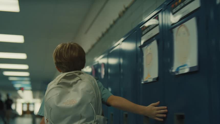 The boy touches all the lockers as he walks down the school hall