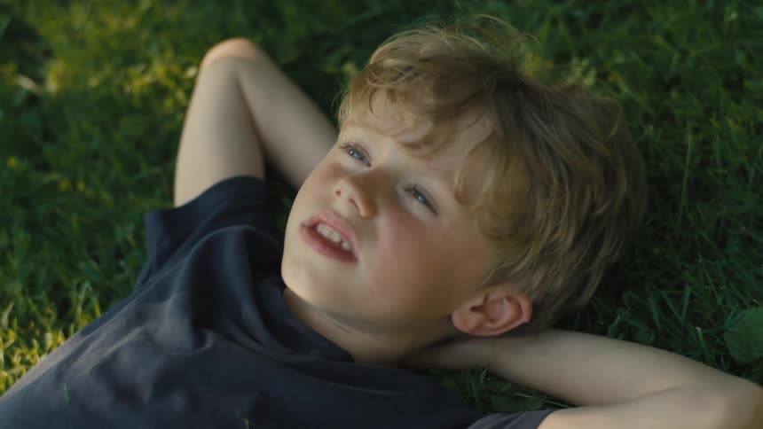 A young boy lies on the grass relaxing in an outdoor park