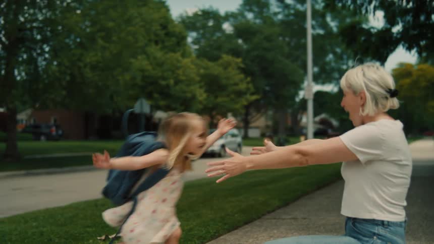 A grandmother and granddaughter walk on a sidewalk together and then hug