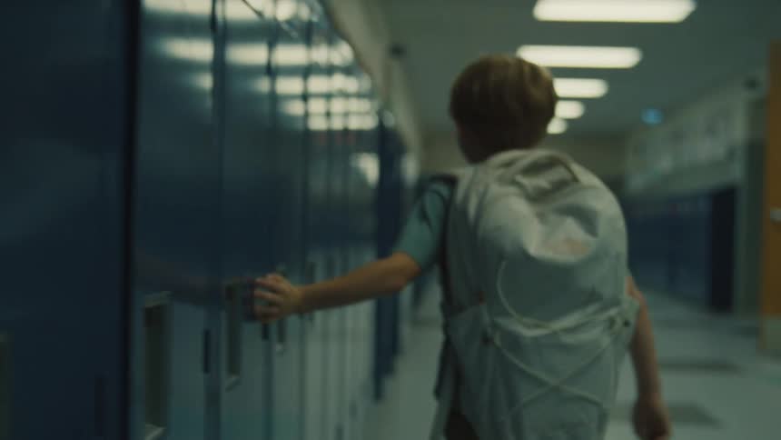 A child with a backpack walks down a school hallway
