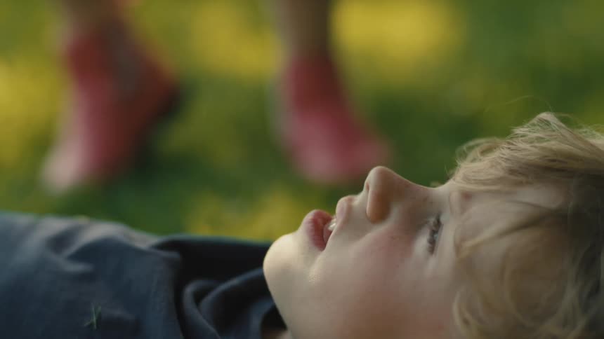 Boy lying on the lawn looks up while another child stands nearby during the day