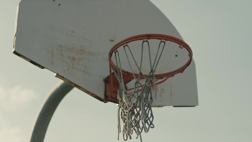 An old weathered basketball hoop with a tattered net stands against a pale sky