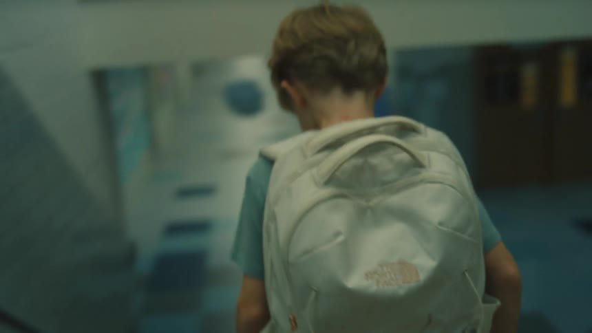 A child with a white backpack viewed from behind as they walk down a staircase in a school hallway