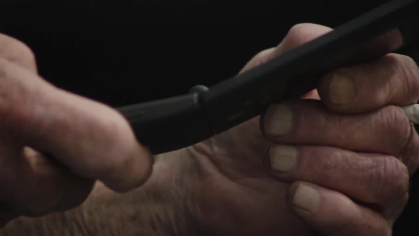 A man texts on his phone while holding a cigarette
