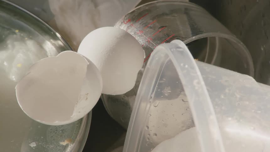 The video shows a kitchen sink filled with dirty dishes there are two eggs and some measuring cups