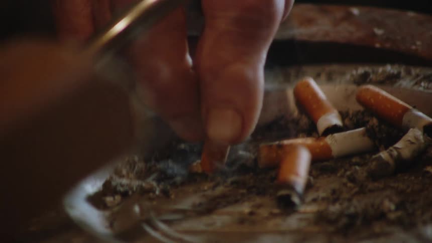 Smoker crushes a burning cigarette in an used metal ashtray