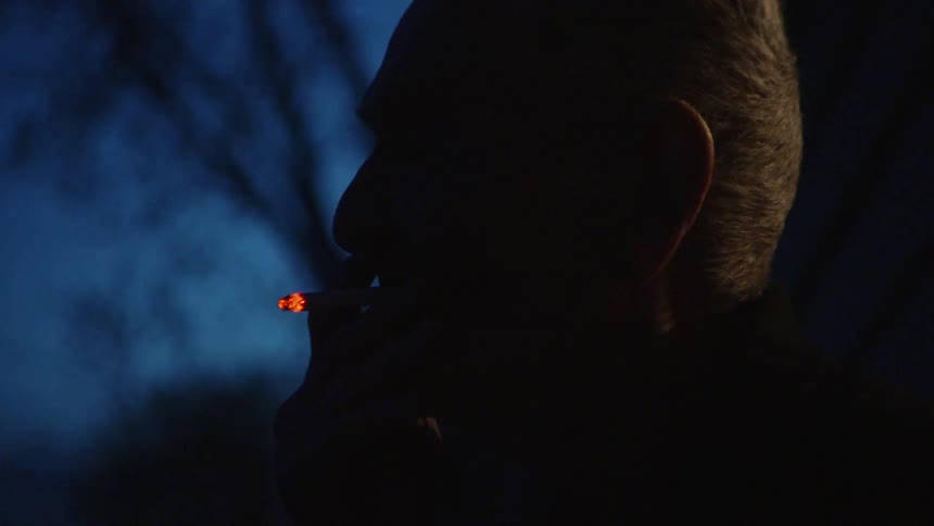 An elderly man smoking outside in the dark of night