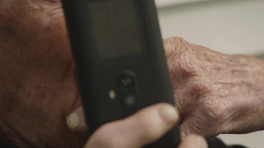 The video shows an elderly man with white hair and a dark shirt he is outdoors and holding a flip phone a closeup shot shows him raising a lit cigarette to his mouth