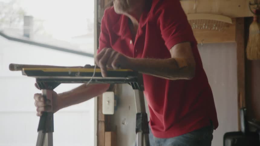 The video shows a man with white hair and a red polo shirt seen in a workshop or garage he is holding what appears to be a tool or piece of equipment and has a cigarette in his mouth