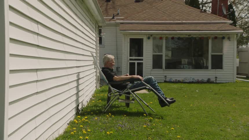 Elderly man relaxes on a reclining chair in the sun in his backyard