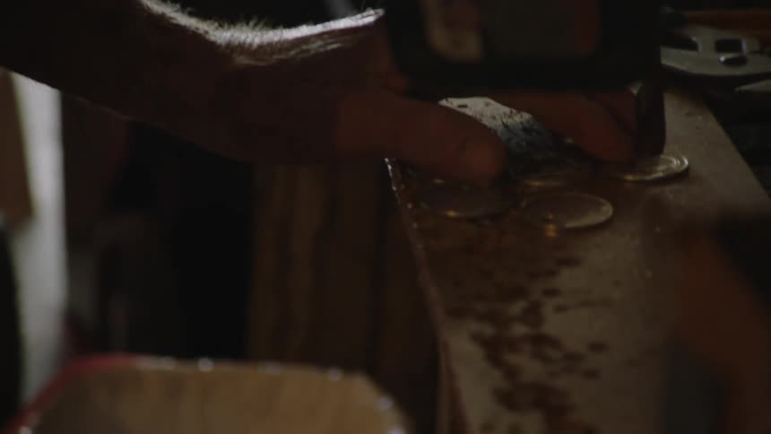 Elderly man drilling metal coins