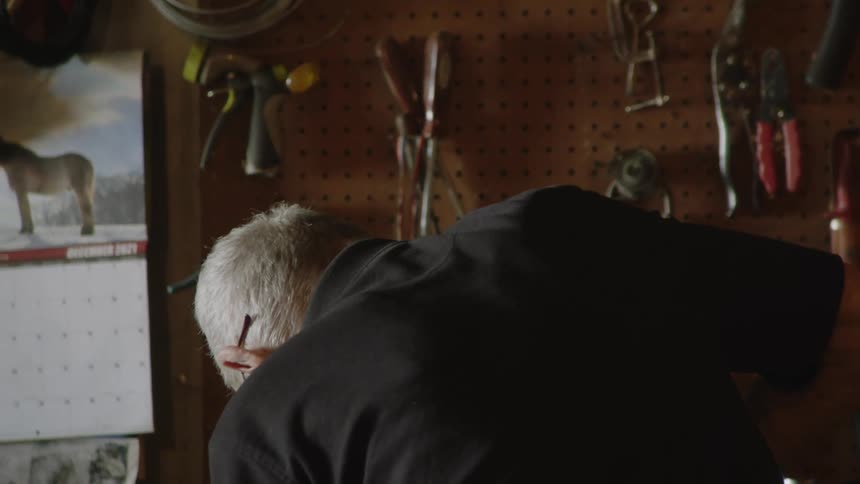 An elderly man works in a dimly lit workshop