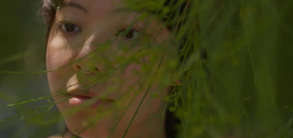 Face of a young woman among green leaves of a tree