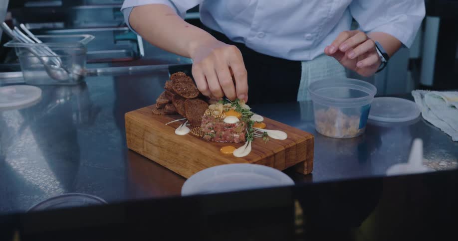 Pair of hands of a person finishing a dish on a wooden board
