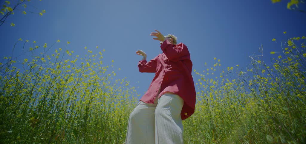 Person dancing in a flower field under an intense blue sky
