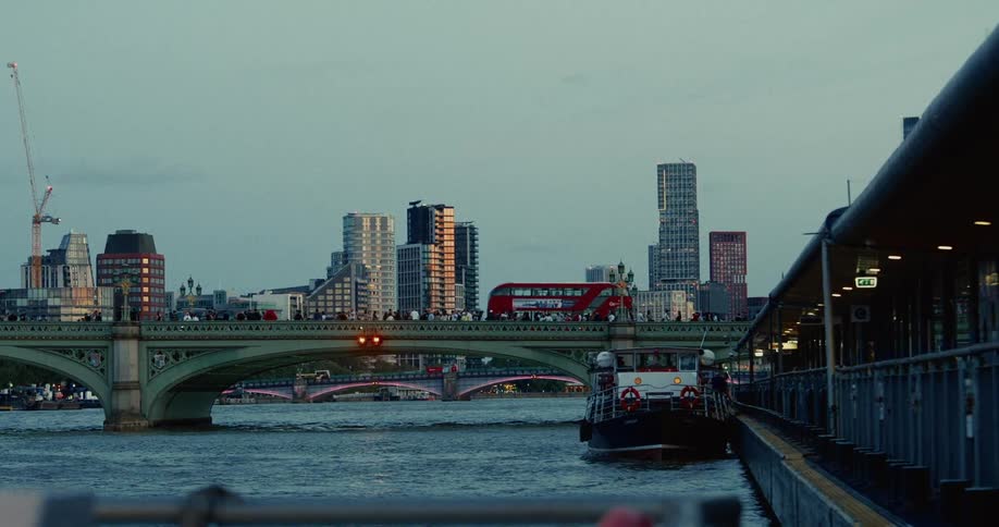 Red bus crosses a bridge over the river thames with london buildings in the background
