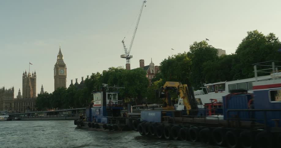 Workboats sail along the river with big ben and the parliament in the background in london
