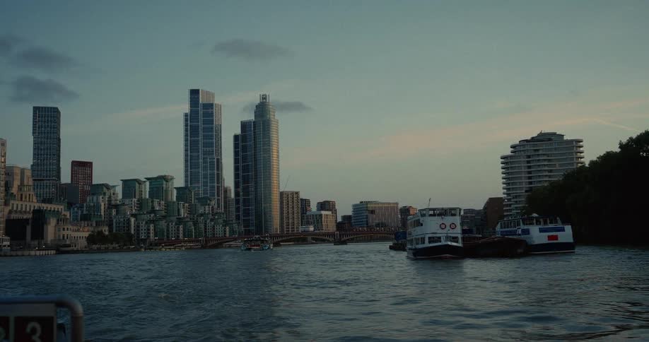 Boats sail on a river surrounded by modern buildings at sunset