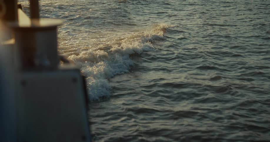 Small waves form behind a boat at sunset