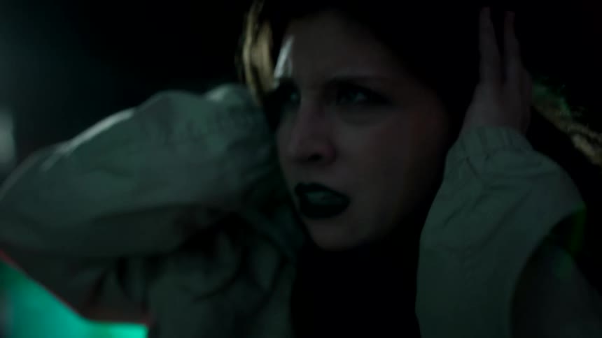 A young woman wearing makeup leans down in fear covering her ears with her hands as a man grabs her from behind taking her hostage and causing panic at night