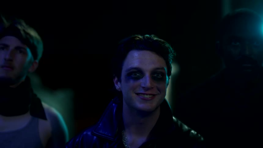 Man in a leather jacket with a bruise on his face stares with a slight smile at night