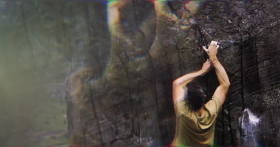 Climber in a yellow shirt ascending a rock wall with chalk marks on his hands