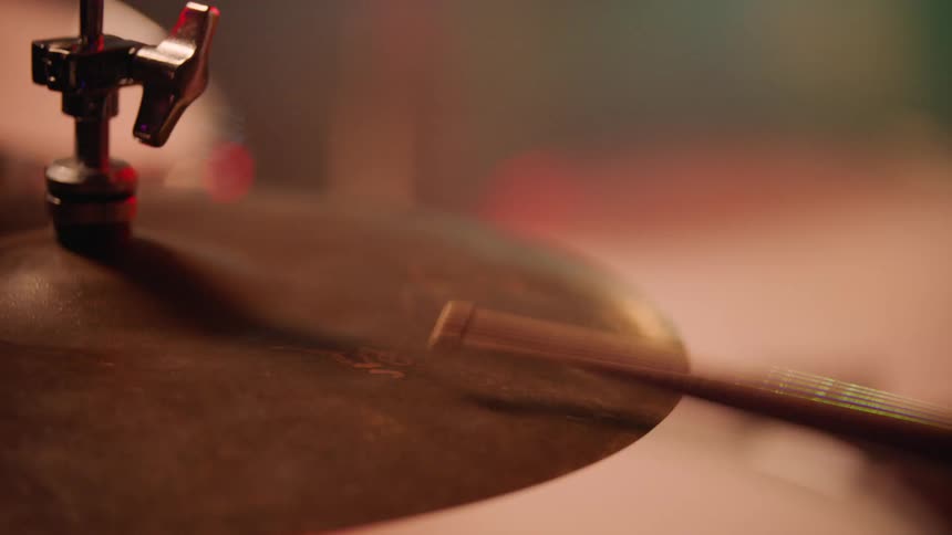 Drummer playing a cymbal with a drumstick in a softly lit environment