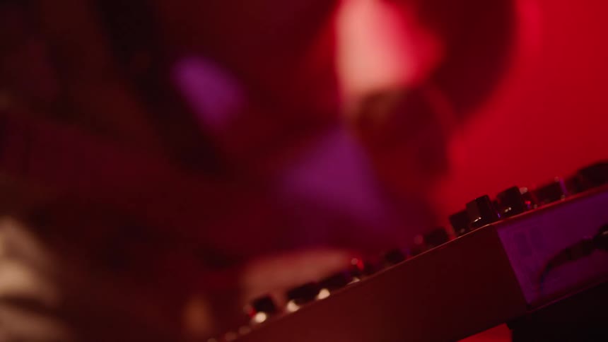 Hand adjusting the controls of an electronic keyboard in a redlit environment