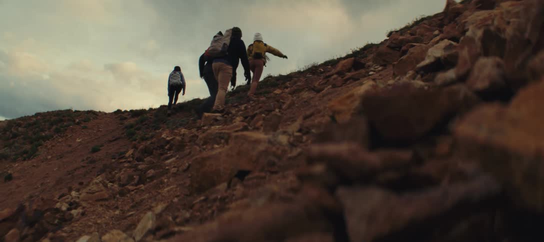 Three people with backpacks climbing a steep rocky trail at sunset