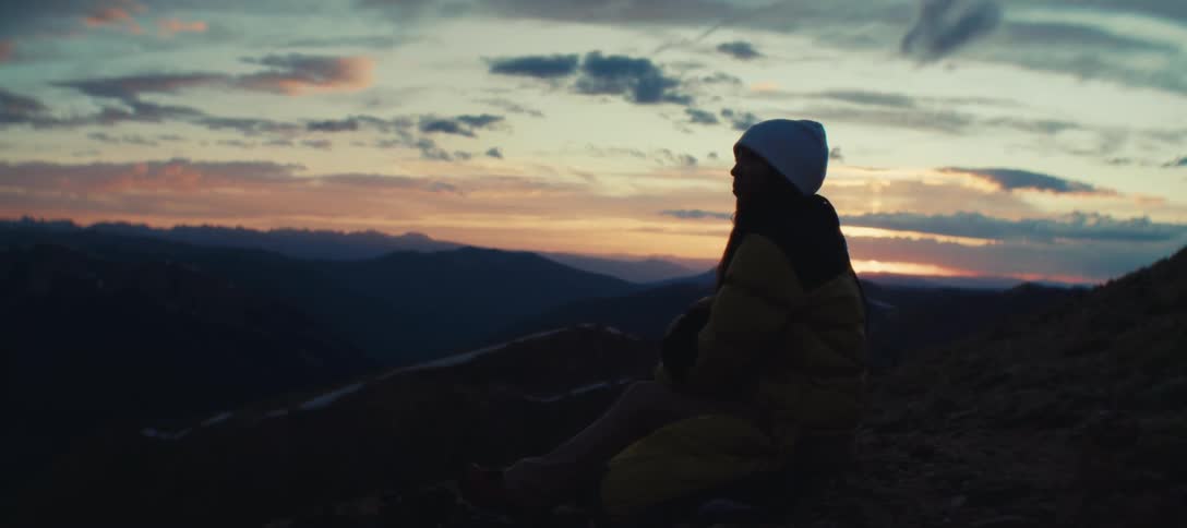 Woman sitting on the slope contemplates the sunset over the mountains