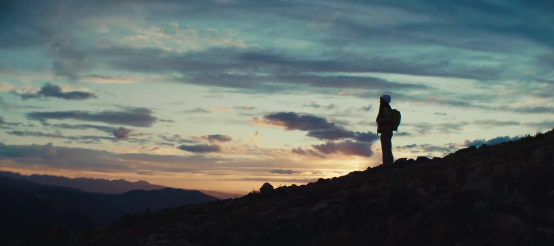 The silhouette of a person walking outdoors on a dark morning with an orange and blue sky and several clouds