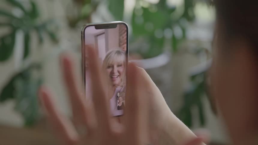 Person waving during a video call on a smartphone with a smiling woman