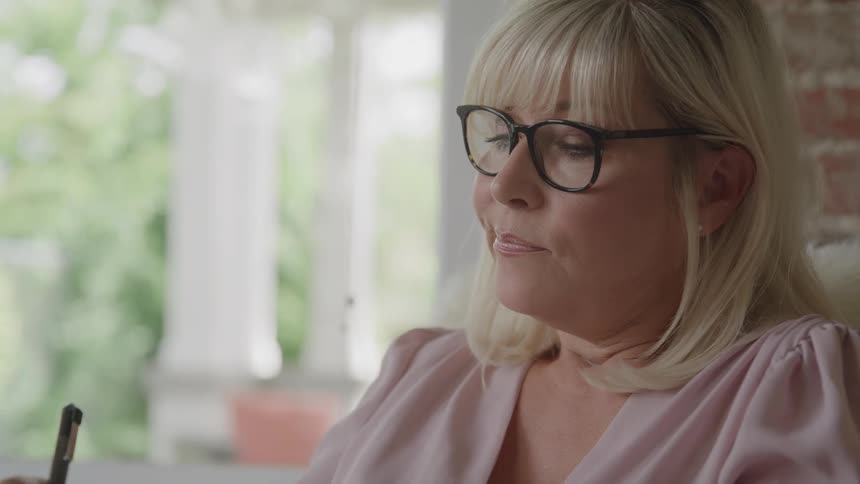 Woman with glasses writes with a focused expression