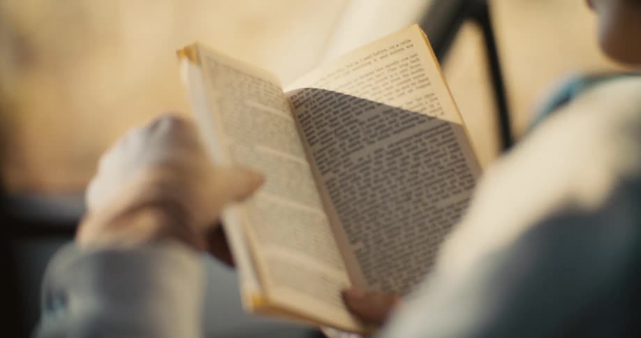 The video shows a blurry closeup of a persons hands and a book or paper they are holding with the text on the pages illegible the scene is bright and backlit making the details hard to distinguish