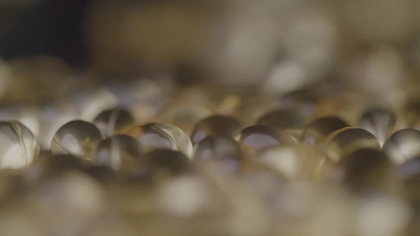 A shallow depthoffield shot slowly pulls focus across a large pile of shiny goldencolored soft gel vitamin capsules