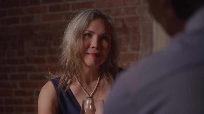 Grayhaired woman wearing a pearl necklace smiles during a conversation in an intimate setting