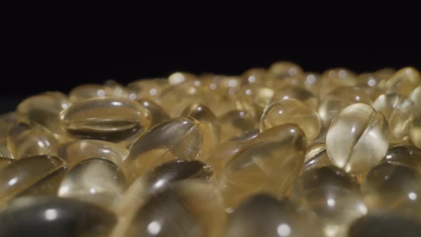A large pile of yellow oblong gelatin capsules resting on a reflective black surface with a plain black background