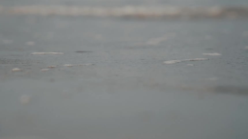 A wide shot of a body of water shows small ripples moving across the surface the sky is overcast and hazy giving the scene a soft muted look