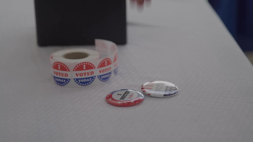 A man picks up a circular voter tag on a table surface