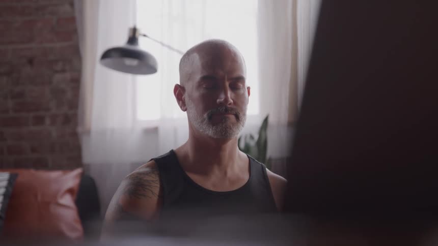A man sits on the floor and meditates with his eyes closed