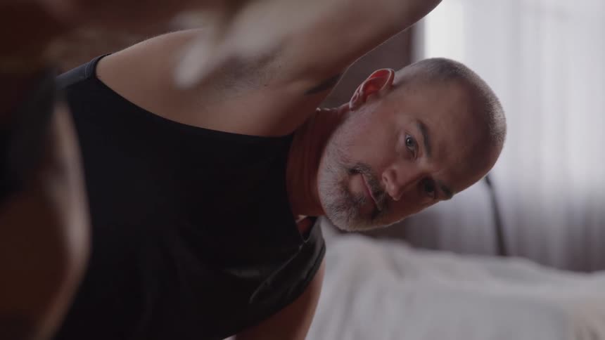 A male yoga practitioner is shown in a wide shot holding a side bend pose he is looking off to the side maintaining his balance and form