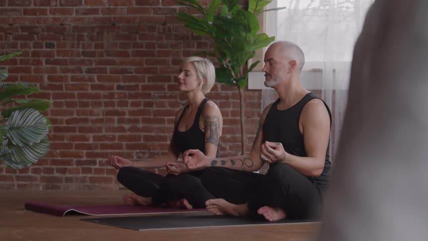 A man and woman sit on yoga mats while meditating with their eyes closed
