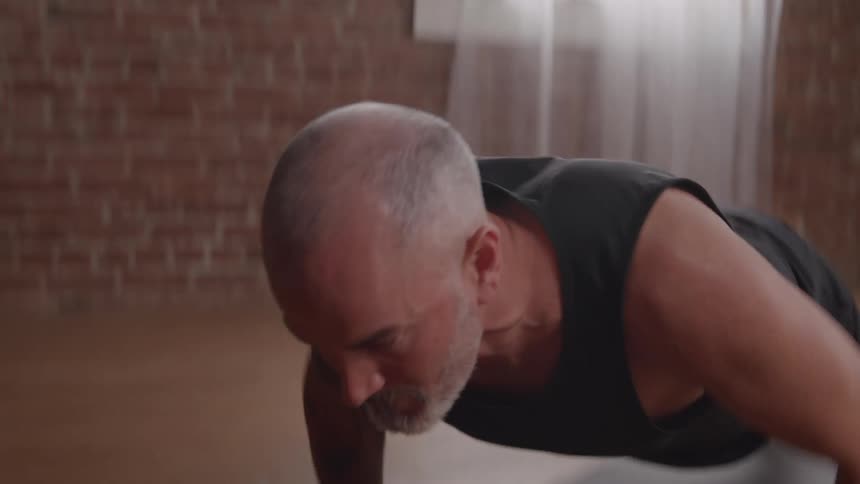 A man performs multiple push ups atop a mat while exercising at home