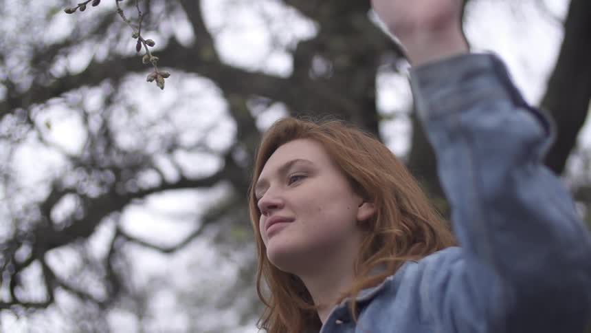 Woman raising her hand in the air with a tree behind her