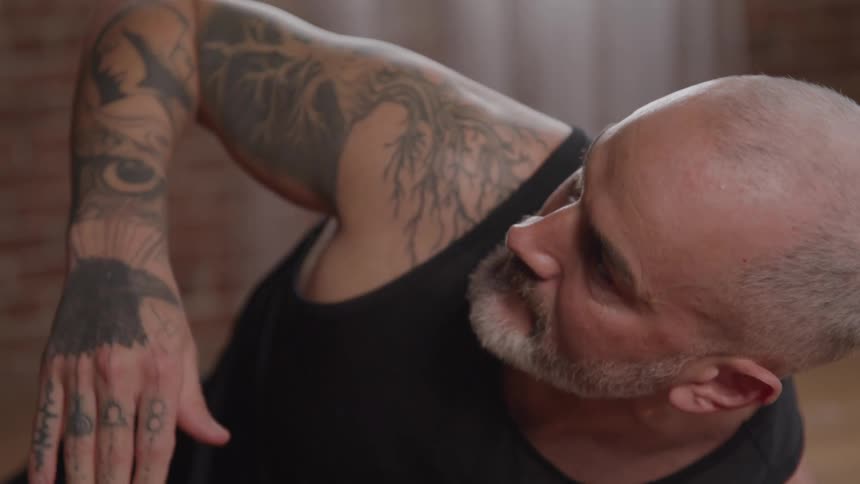 Tattooed graybearded man doing stretching exercise