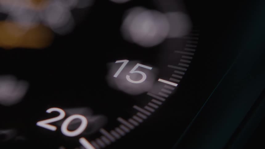 A dark clock with a yellow needle spinning around the dial